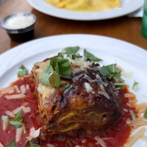 A delicious lasagna with rich red sauce, fresh basil, and grated cheese on a white plate.