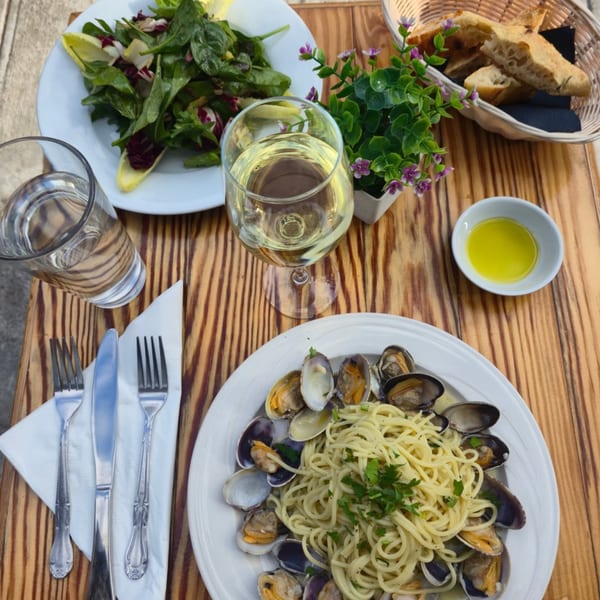 Italian meal with spaghetti alle vongole, a green salad, bread, white wine, and olive oil on a wooden table.