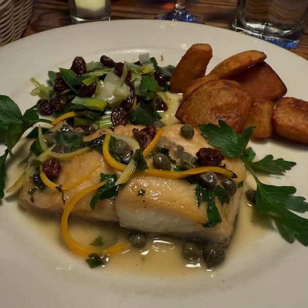 Italian fish dish with lemon, capers, parsley, leeks, raisins, and fried potatoes on a white plate.