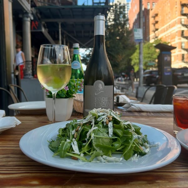 Arugula salad with pine nuts and cheese, white wine, and a wine bottle on an outdoor table.