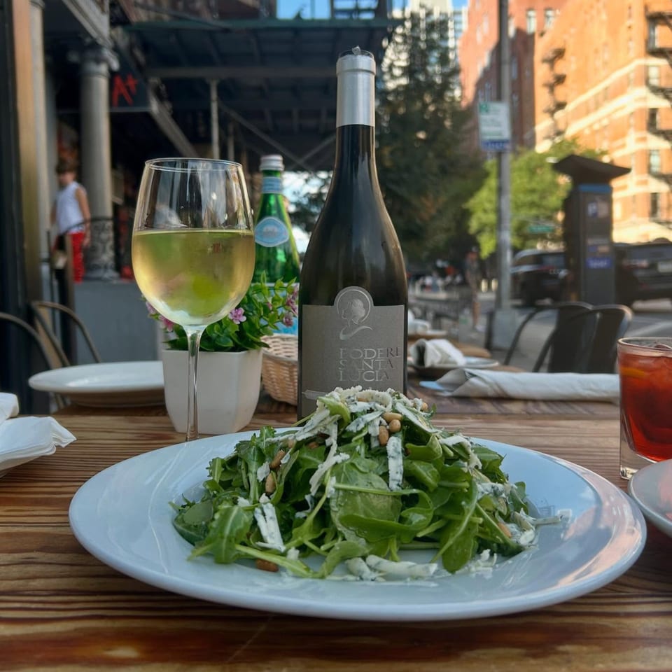 Arugula salad with pine nuts and cheese, white wine, and a wine bottle on an outdoor table.